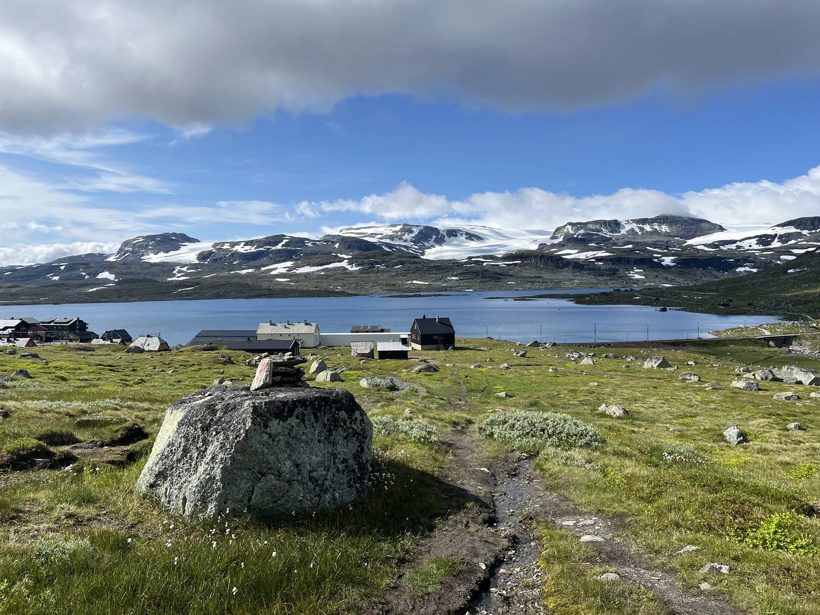 Snowy mountain tops behind a blue lake and green grass in Norway